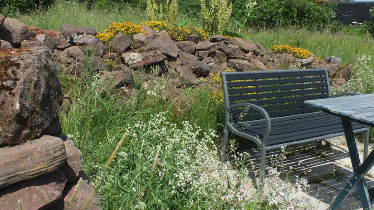 Een gezellige tuin met een bank en een tafel. Groene weiden en kleurrijke bloemen omringen de stenen.