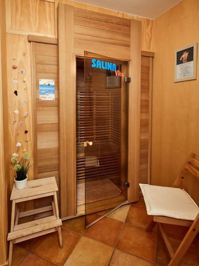 Ein gemütlicher Wellnessbereich mit einer gläsernen Tür zu einer Sauna. Die Wände sind aus Holz und es gibt eine kleine Sitzecke.