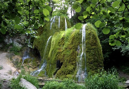 De Dreim&uuml;hlen-waterval in het midden tussen dicht gras en groene bomen.