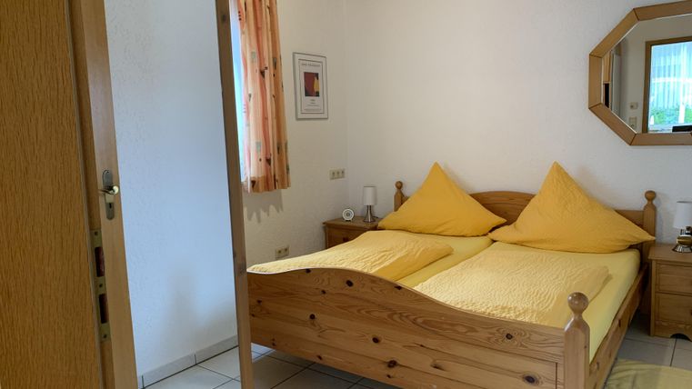 Ein gemütliches Schlafzimmer mit einem Doppelbett und gelben Kissen. Die Wände sind hell und es gibt Fenster mit Vorhängen.