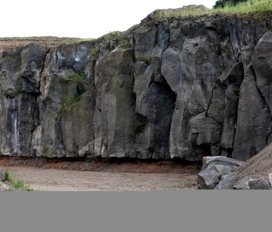 A quarry with high, jagged rock faces. Earth and grass can be seen in the foreground, vegetation grows on the rocks above., © Touristik GmbH Gerolsteiner Land