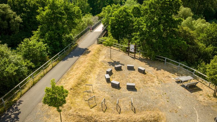 Rustplaats aan de Kyll-fietsroute in Stadtkyll met banken en een tafel, omringd door groene bomen en een fietspad.