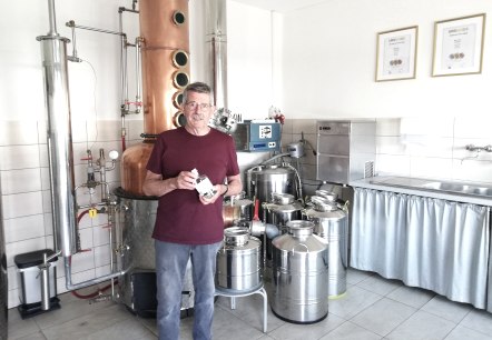 Ein Mann vor einer Destilliermaschine mit einer Flasche Gin in der Hand.