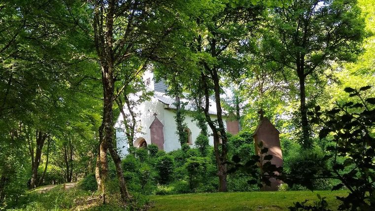 Eine kleine Kapelle verborgen im dichten Grün eines Waldes. Die Umgebung ist friedlich und einladend.