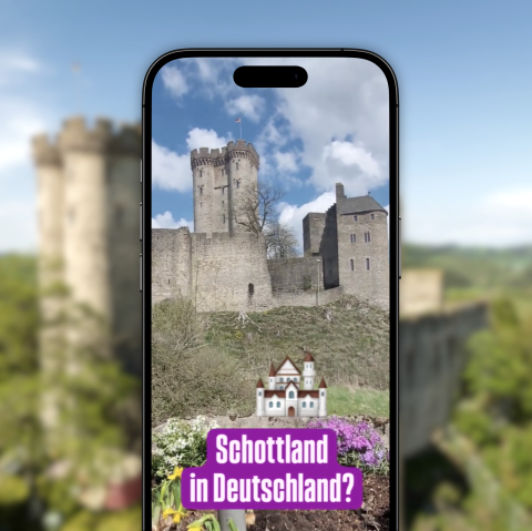 Vor dem verschwommenen Hintergrund ist ein Handy, welches auf Instagram das Reel zum Wanderweg Felsenpfad zeigt.