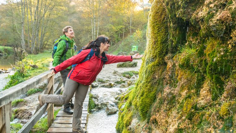 Deux personnes observent la cascade recouverte de mousse et s'approchent de l'eau.