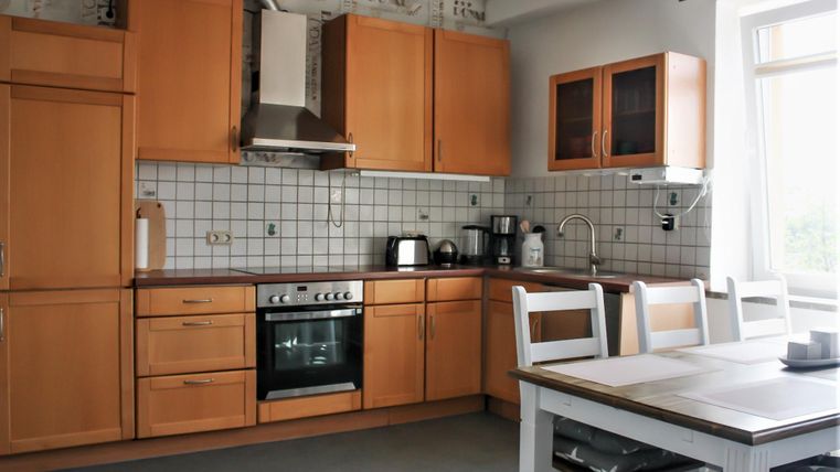 Eine moderne Küche mit Holzschränken und einem weißen Tisch. Der Raum ist hell und gut ausgestattet.