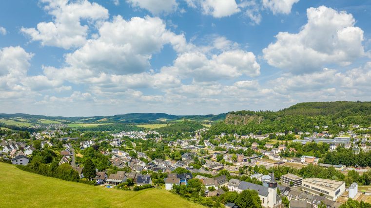 Panoramablick auf Gerolstein mit grünen Hügeln, Häusern und bewölktem Himmel. Im Hintergrund sind die Dolomiten zu sehen.