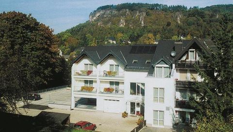 Ein modernes Gebäude mit mehreren Stockwerken und Balkonen. Im Hintergrund erkennt man einen bewaldeten Hang.