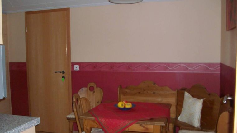 Ein gemütlicher Essbereich mit Holzmöbeln und einer roten Tischdecke. An dem Tisch liegt eine Obstschale und die Wände sind in sanften Farben gestrichen.