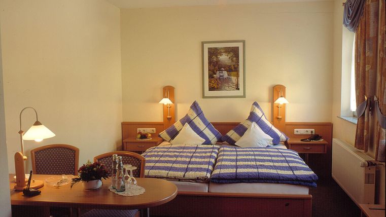 Ein gemütliches Hotelzimmer mit einem Doppelbett und karierten Kissen. Der Raum verfügt über einen Tisch, einen Stuhl und eine angenehme Beleuchtung.