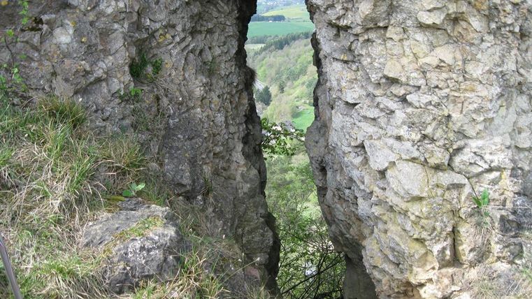 Ein natürlicher Felsspalt mit grasbewachsenen Ufern. Durch die Öffnung blickt man auf eine grüne Landschaft.