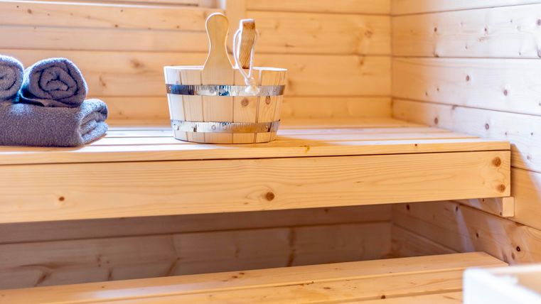 Un sauna confortable avec des murs en bois. Sur l'étagère se trouvent des serviettes et un récipient en bois.