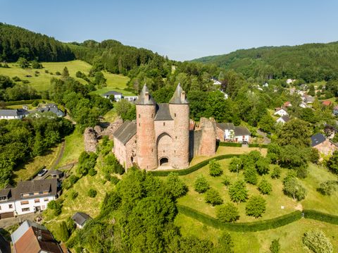 Aerial view of Bertrada Castle in Mürlenbach, surrounded by green countryside and houses.