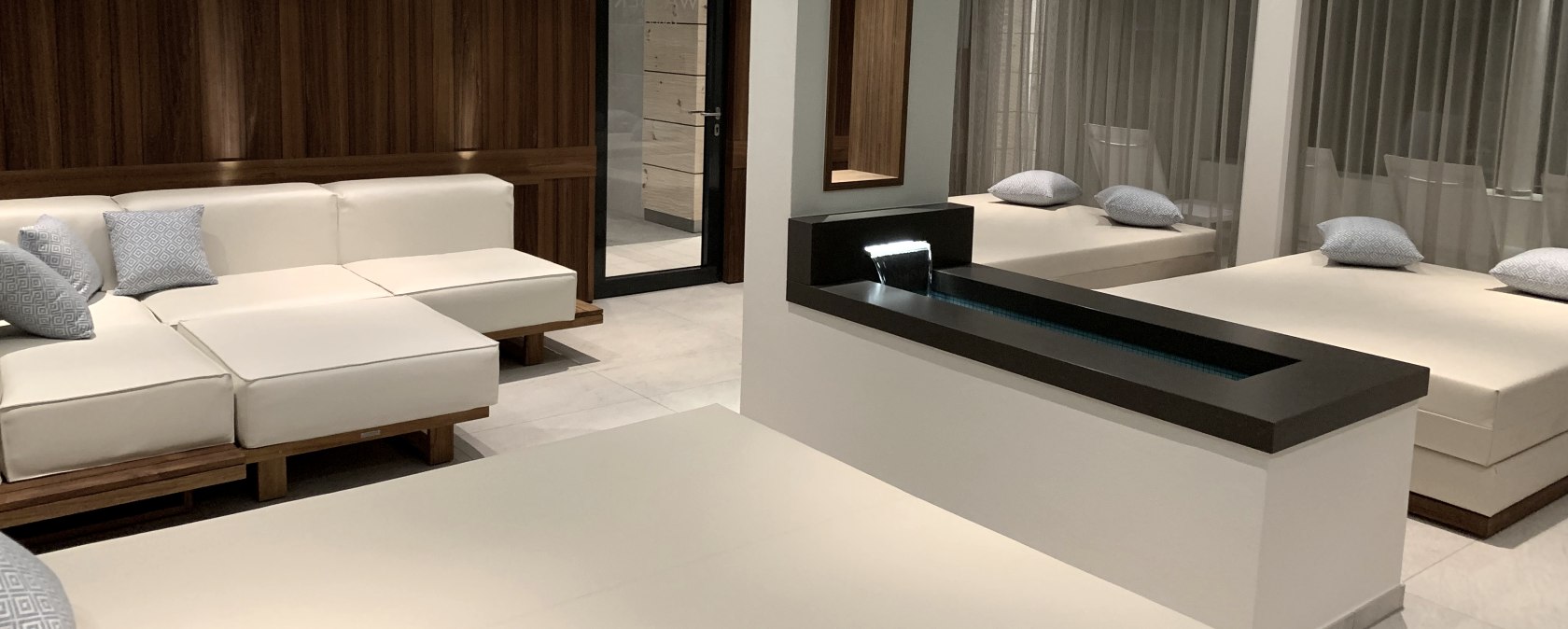 Mehrere stirile Liegen und Sofas in einem Raum verteilt. In der Mitte ein kleines Wasserbecken.