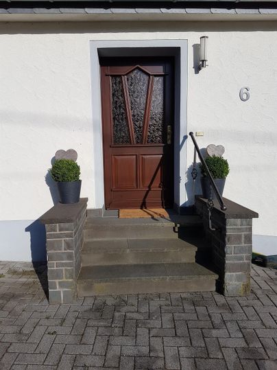Eine Haustür aus Holz mit gläsernen Elementen. Die Treppe ist mit Töpfen und Pflanzen dekoriert.