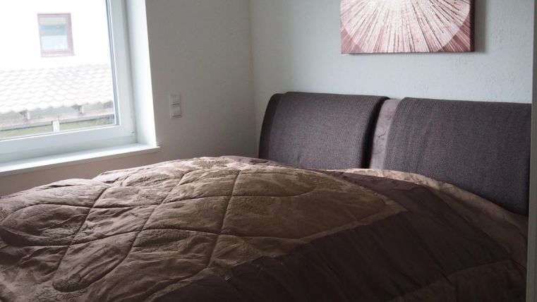 Ein gemütliches Schlafzimmer mit einem großen Bett und einem modernen Wandbild. Das Zimmer hat ein Fenster, das Tageslicht hereinlässt.