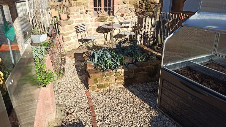 Un petit jardin pavé avec un jardin de pierres et un potager. À l'arrière-plan, il y a deux chaises et une table.