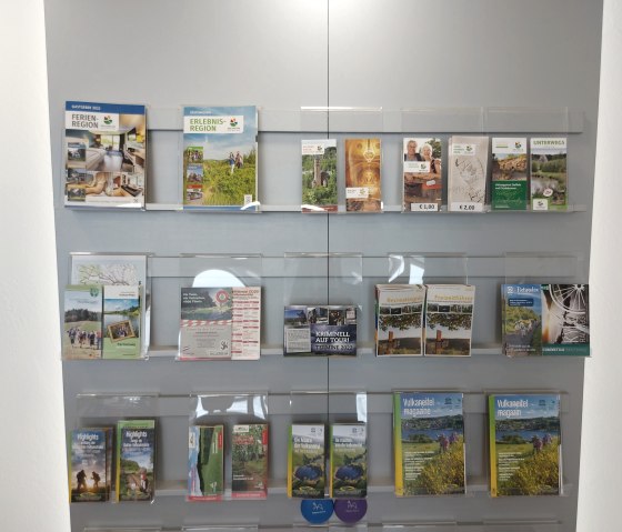 Interieur van het toeristeninformatiecentrum Stadtkyll met een brochurewand waarop talrijke toeristische drukwerken worden tentoongesteld.