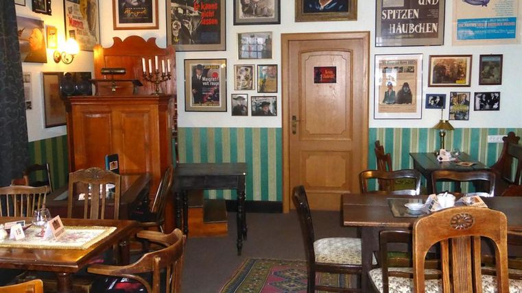 Gemütlicher Raum mit Holzmöbeln, grünen Wänden und zahlreichen Filmplakaten. Ein Teppich liegt auf dem Boden, und ein Schrank steht in der Ecke.