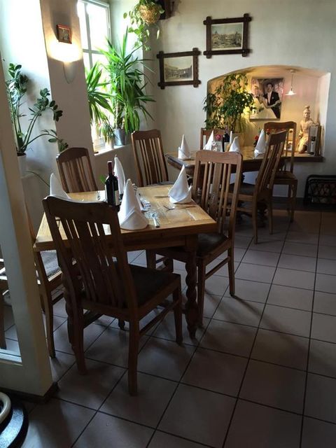 Ein gemütliches Restaurant mit Holztischen und -stühlen, weißen Servietten, Pflanzen und Wandbildern. Ein einladender, heller Raum.