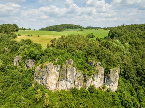 Felsen der Gerolsteiner Dolomiten umgeben von grünen Wäldern und Wiesen unter einem bewölkten Himmel.