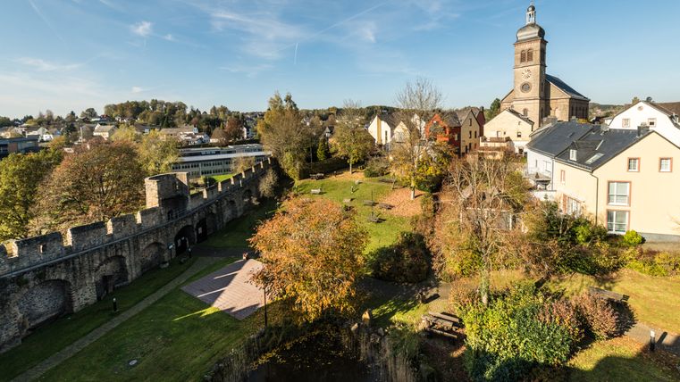 Blick auf Hillesheim mit Stadtmauer und Kirche im Hintergrund.