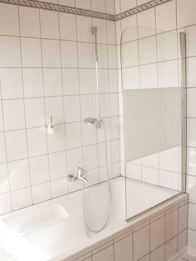 Ein modernes Badezimmer mit einer Badewanne und einer Glasduschabtrennung. Die Wände sind mit weißen Fliesen gestaltet.