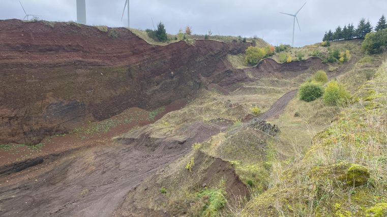 Ici, on a une vue sur le volcan. On aperçoit des collines légèrement couvertes de végétation. Le ciel est nuageux.