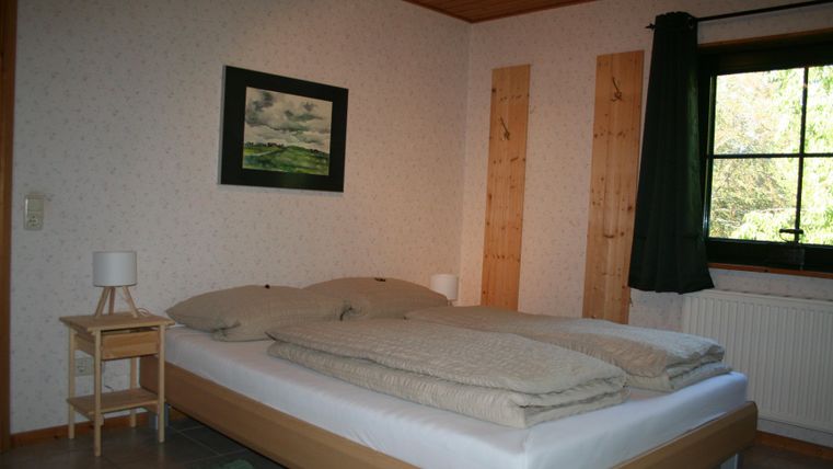 Een gezellige slaapkamer met een groot bed en houtbekleding.
Aan de muur hangt een schilderij en een raam zorgt voor daglicht.