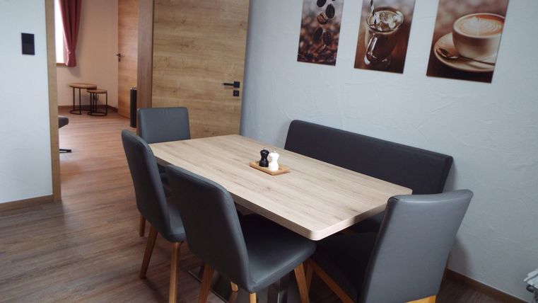 Ein moderner Essbereich mit einem Holztisch und grauen Stühlen. An der Wand hängen Bilder von Kaffee und Kaffeebohnen.