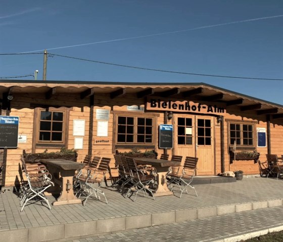 Wooden building of the Bielenhof-Alm with tables and chairs outside under a clear sky., &copy; Touristik GmbH Gerolsteiner Land