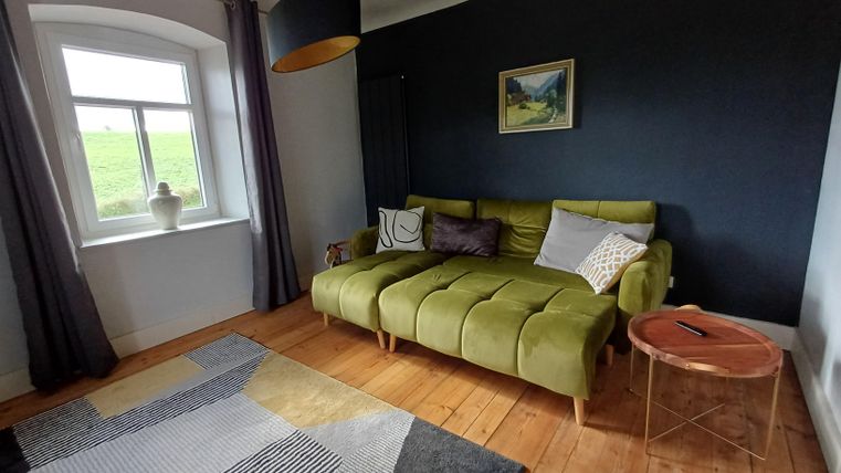 Een moderne woonkamer met een groene bank en een kleine tafel. Aan de muur hangt een schilderij en de vloer is van hout.