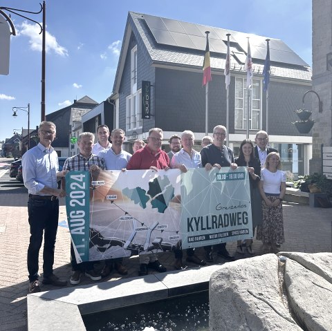 13 Personen stehen dicht beieinander und halten ein Veranstaltungsbanner f&uuml;r den Radaktionstga Grenzenlos kyllradweg am 11. August 2024 hoch.