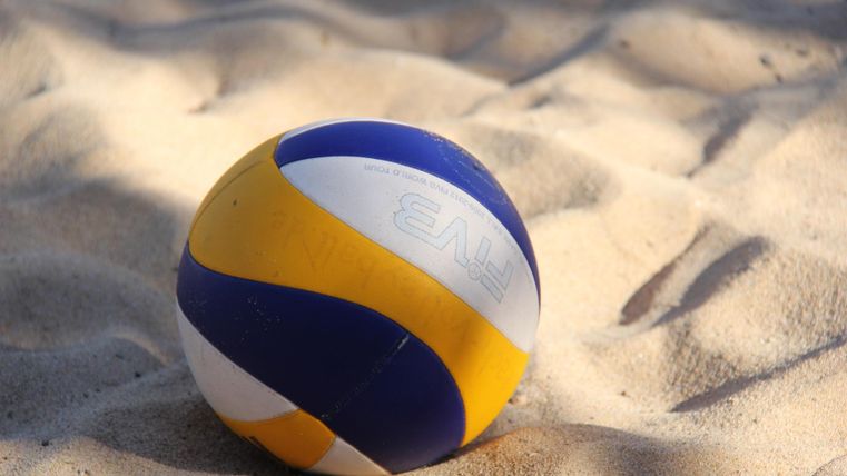 Ein blau, gelb und weiß gestreifter Volleyball liegt auf einer Sandfläche.