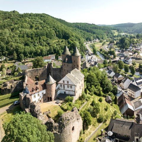 Blick von oben auf das Dorf M&uuml;rlenbach, durch das quer der Fluss Kyll flie&szlig;t und auf einer Anh&ouml;he trohnt die historische Bertradaburg. 