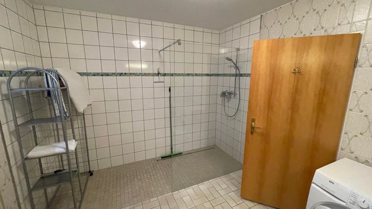 Une salle de bain simple avec des murs carrelés et un espace douche. À gauche se trouve un séchoir à linge et à droite se trouve une machine à laver.