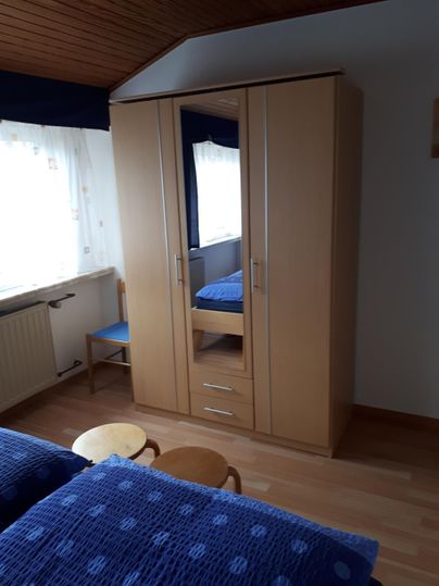 Ein gemütliches Schlafzimmer mit einem großen Holzschrank und zwei Einzelbetten. Das Licht fällt durch ein Fenster, das den Raum freundlich und einladend macht.