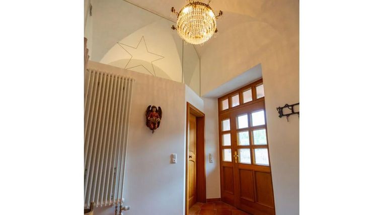 Ein einladender Eingangsbereich mit warmen Terrakottaboden und charmanten Holzdetails. Eine elegante Deckenlampe sorgt für angenehmes Licht.