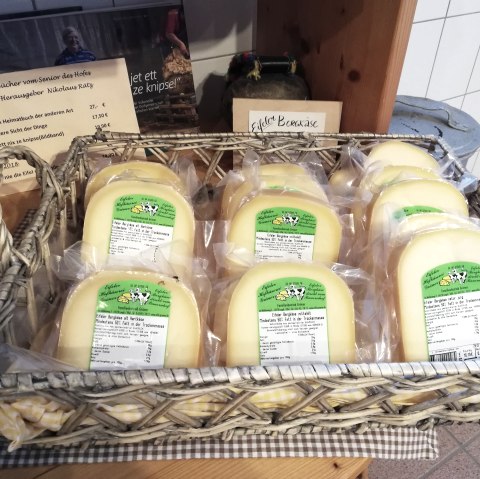 A wooden basket filled with several shrink-wrapped pieces of cheese from the Gröner Hof brand.