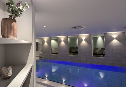 An indoor pool with blue water in a warmly lit spa room.