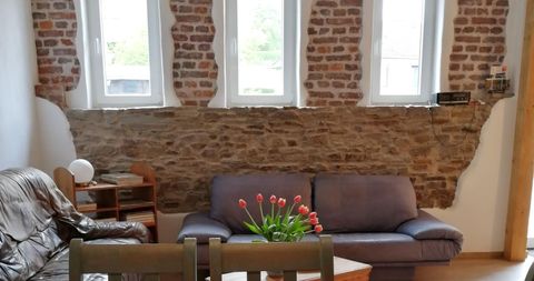 Een gezellige woonkamerinrichting met een bakstenen muur en grote ramen. Een bank en een tafel met een bloemenvaas creëren een uitnodigende sfeer.