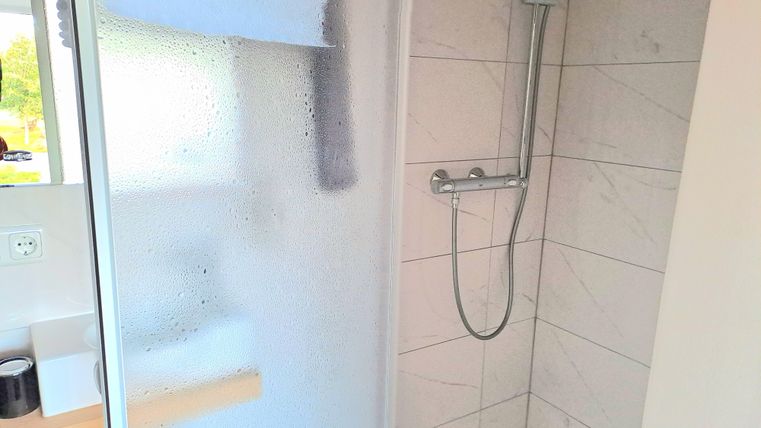 Eine moderne Dusche mit gläserner Tür und Wassertropfen auf der Oberfläche. Der Raum ist hell und freundlich gestaltet.