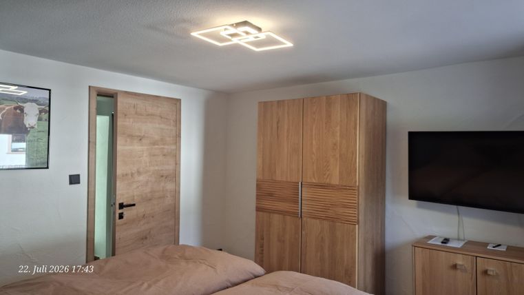 Ein modernes Schlafzimmer mit einem Doppelbett, einem Holzschrank und einem Fernseher. An der Wand befindet sich eine Tür und ein dekoratives Bild.