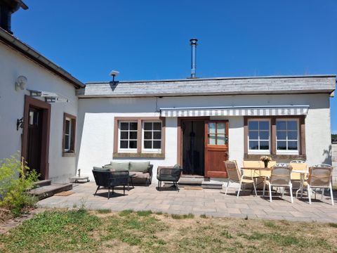 Ein gemütliches Haus mit einer Terrasse und einem Garten. Der Himmel ist klar und blau, ideal für entspannte Tage im Freien.