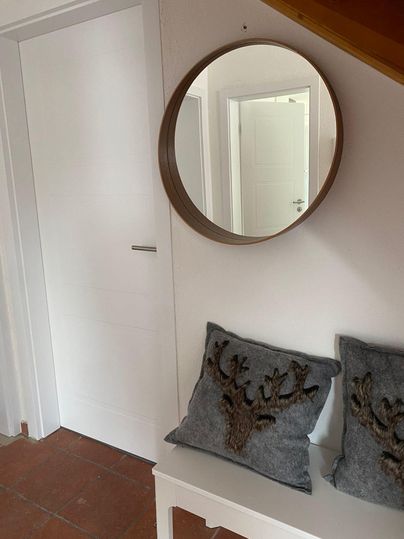 Ein gemütlicher Flur mit einem runden Spiegel an der Wand. Zwei dekorative Kissen auf einer weißen Bank verleihen dem Raum eine einladende Atmosphäre.