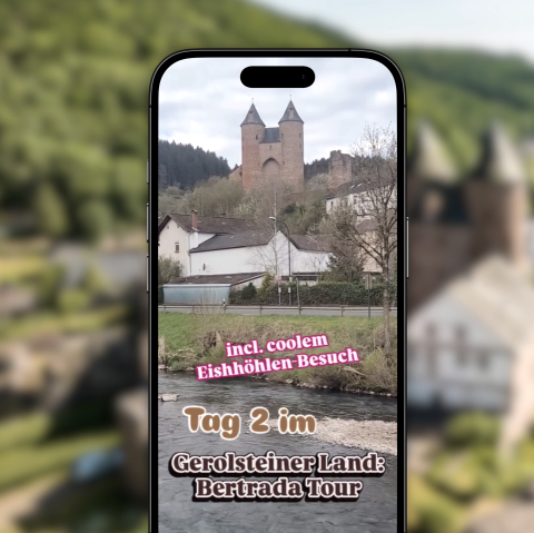 Vor dem verschwommenen Hintergrund ist ein Handy, welches auf Instagram das Reel zum Wanderweg Bertradatour zeigt.