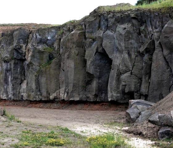 A quarry with high, jagged rock faces. Earth and grass can be seen in the foreground, vegetation grows on the rocks above., © Touristik GmbH Gerolsteiner Land