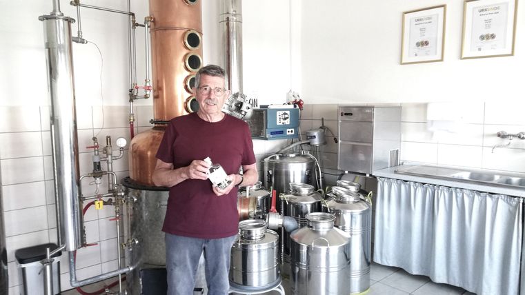 Ein Mann vor einer Destilliermaschine mit einer Flasche Gin in der Hand.