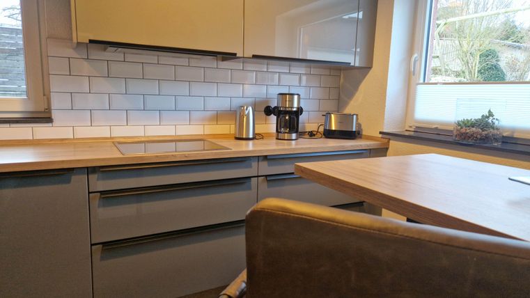 Eine moderne Küche mit grauen Schränken und Holzarbeitsfläche. Auf dem Tisch steht ein Stuhl und es gibt verschiedene Küchengeräte auf der Arbeitsplatte.